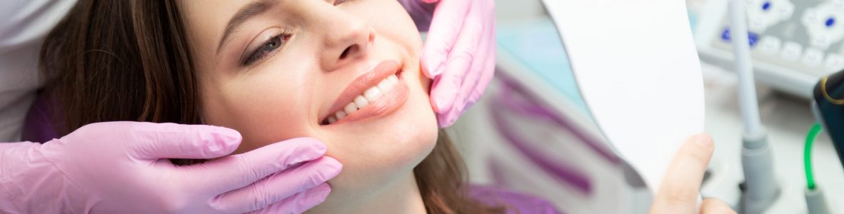 Happy patient after tooth treatment at dental clinic. Smiling girl with white well-groomed teeth after taking doctor help. Satisfied lady look at mirror enjoy healthy enamel after whitening procedure