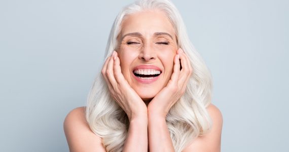 Close-up portrait of her she nice attractive excited cheerful grey-haired elderly lady touching cheeks laughing isolated gray pastel color background.