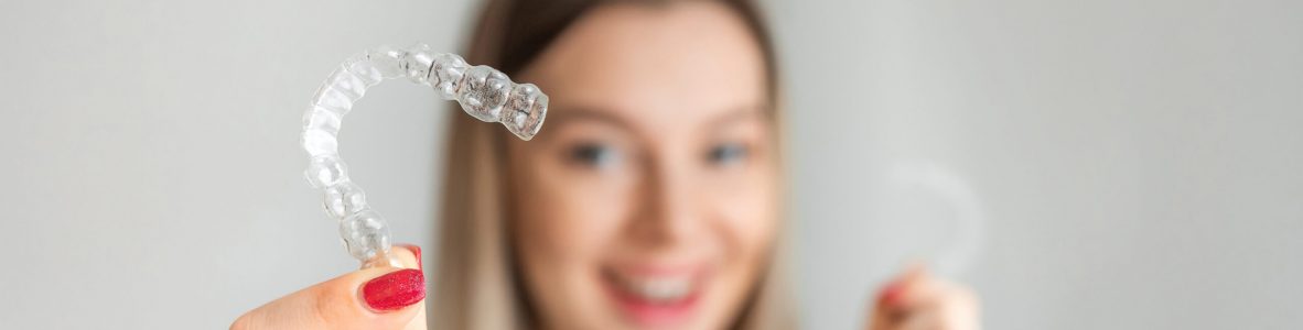 Female hand holding Invisalign, the invisible braces aligner at face woman background. Correction of teeth concept