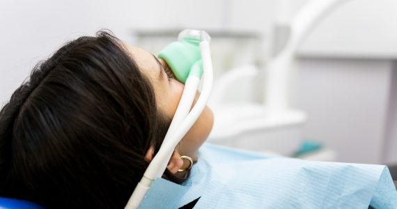 An adult woman sits in a dentist's clinic wearing a nasal mask to inhale nitrous oxide. Dentist fear concept. Feeling of relaxation with laughing gas.